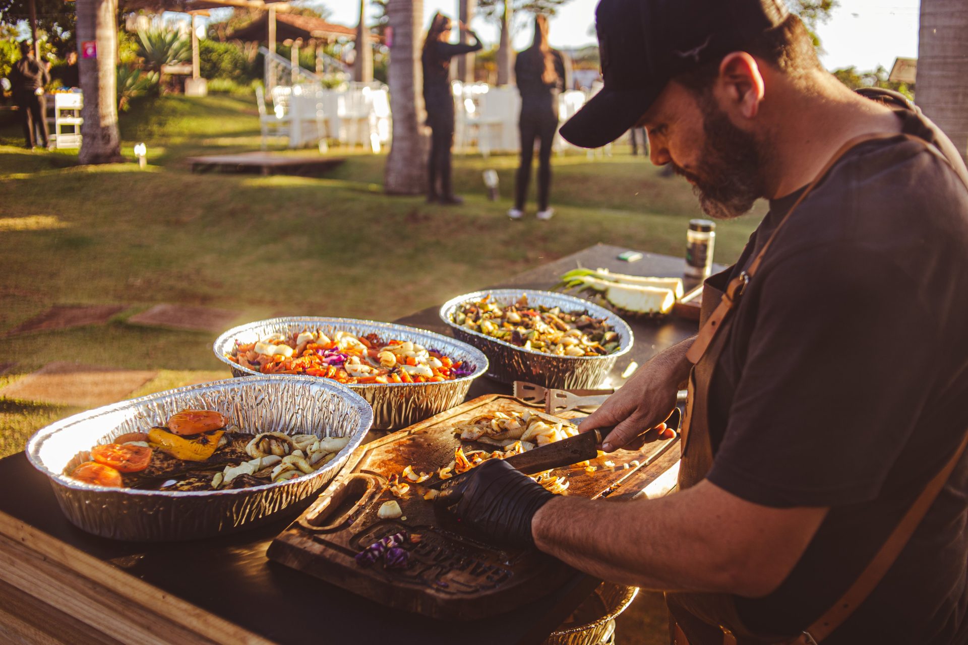 Chef preparing grilled vegetables at an outdoor event with natural lighting and festive atmosphere.